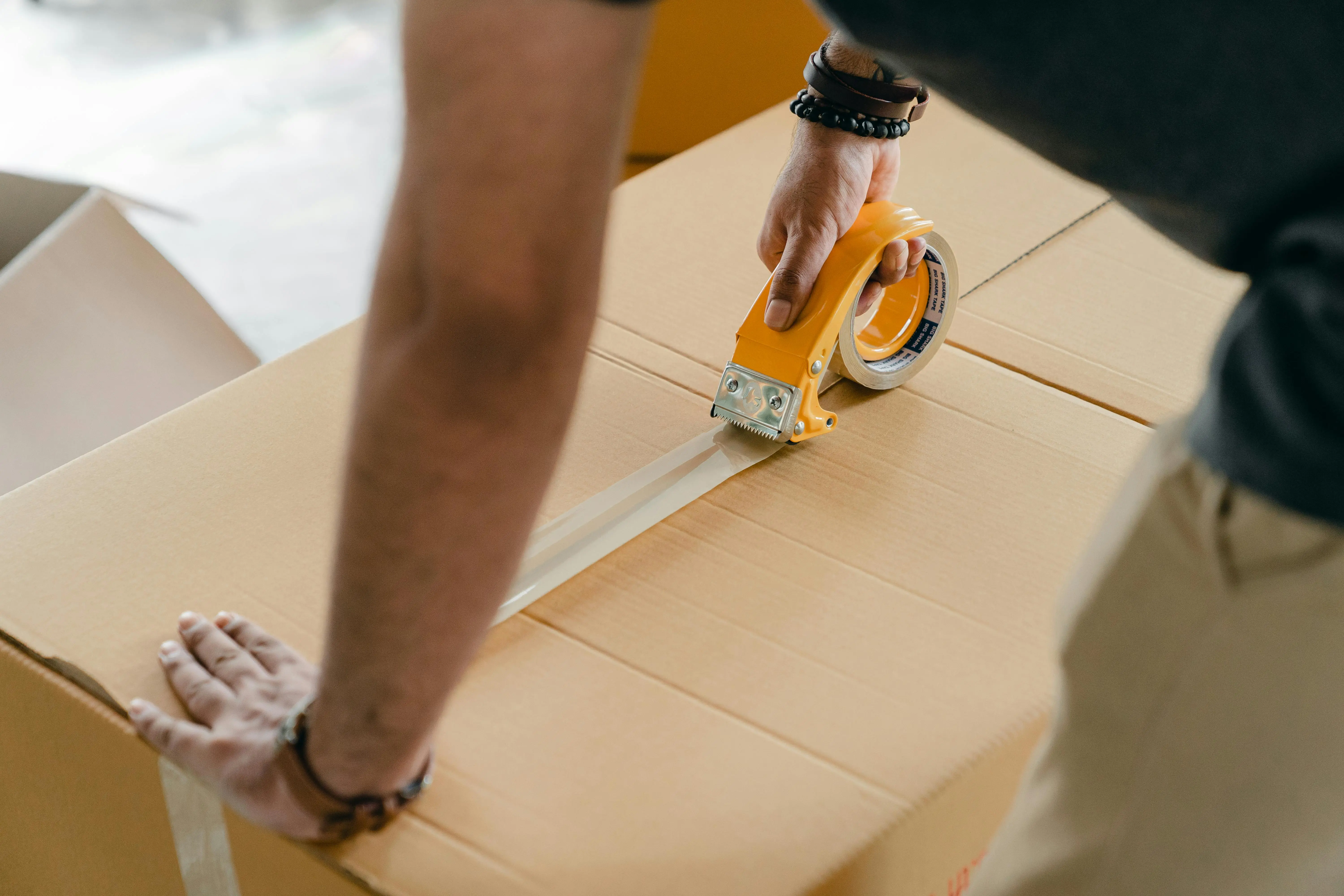 person using packing tape to close a box of moving items.